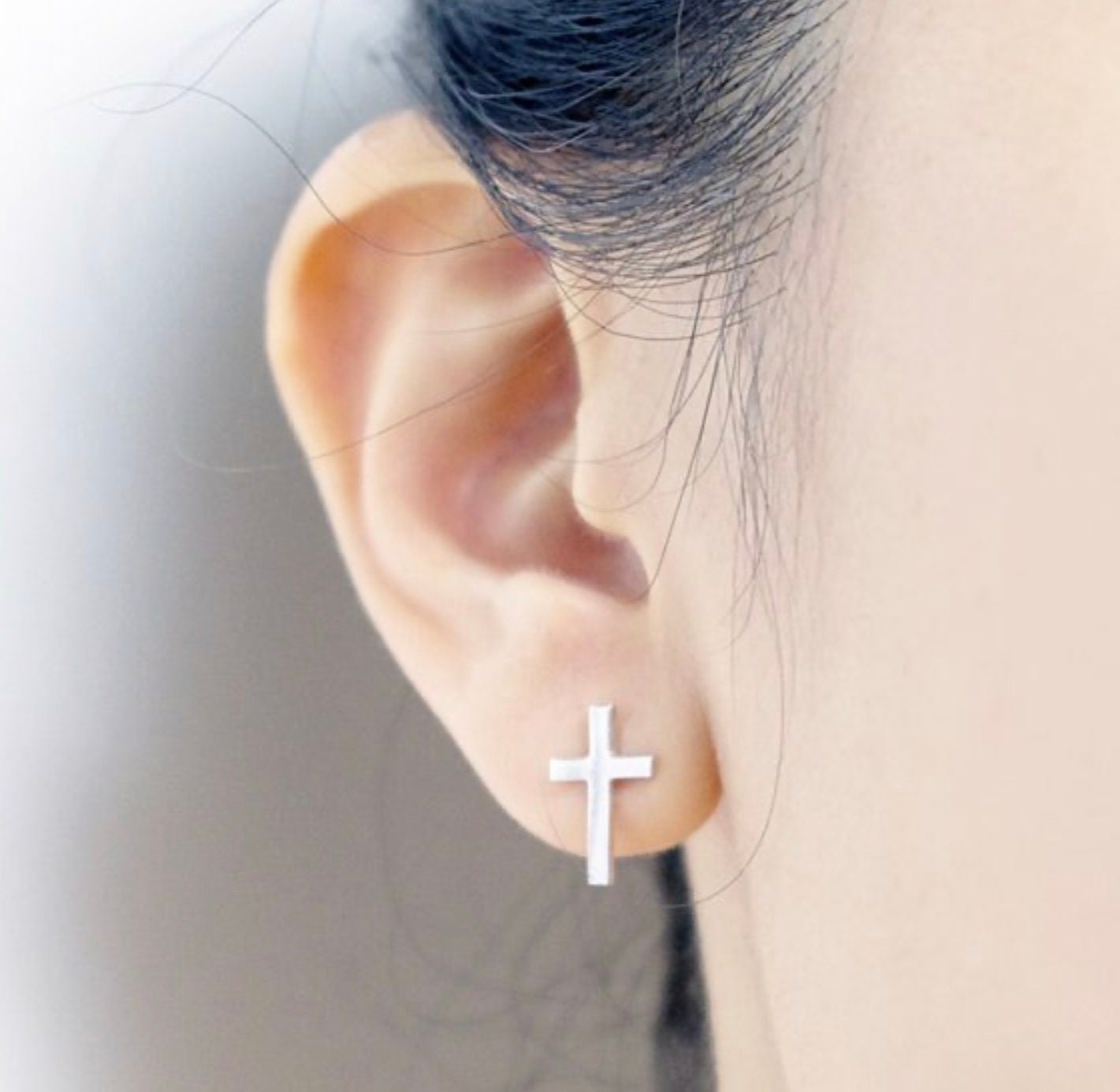 Silver cross stud earrings on ear with post backs