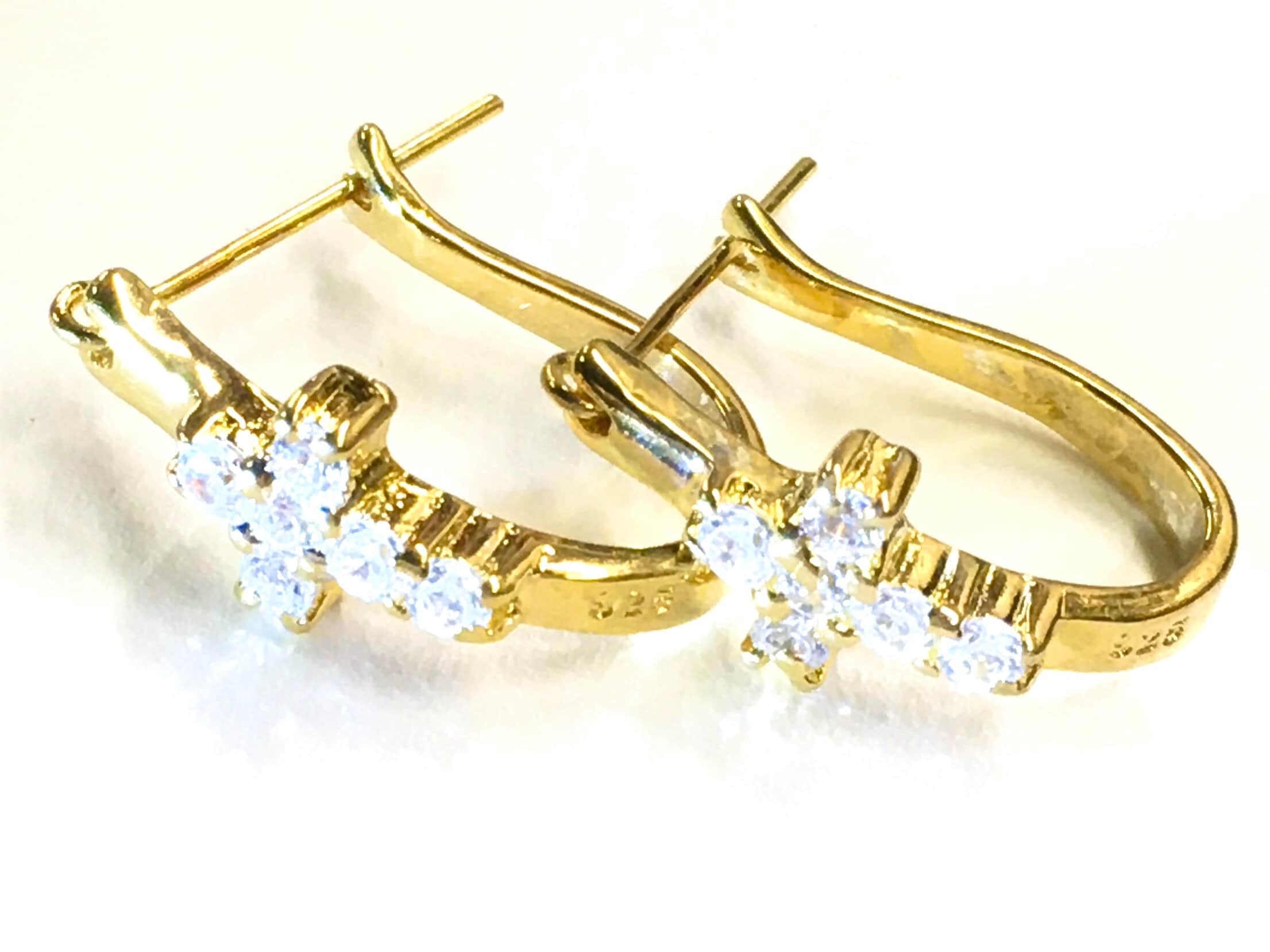 Gold-tone cross huggie earrings with clear CZ stones, flat lay on light background.