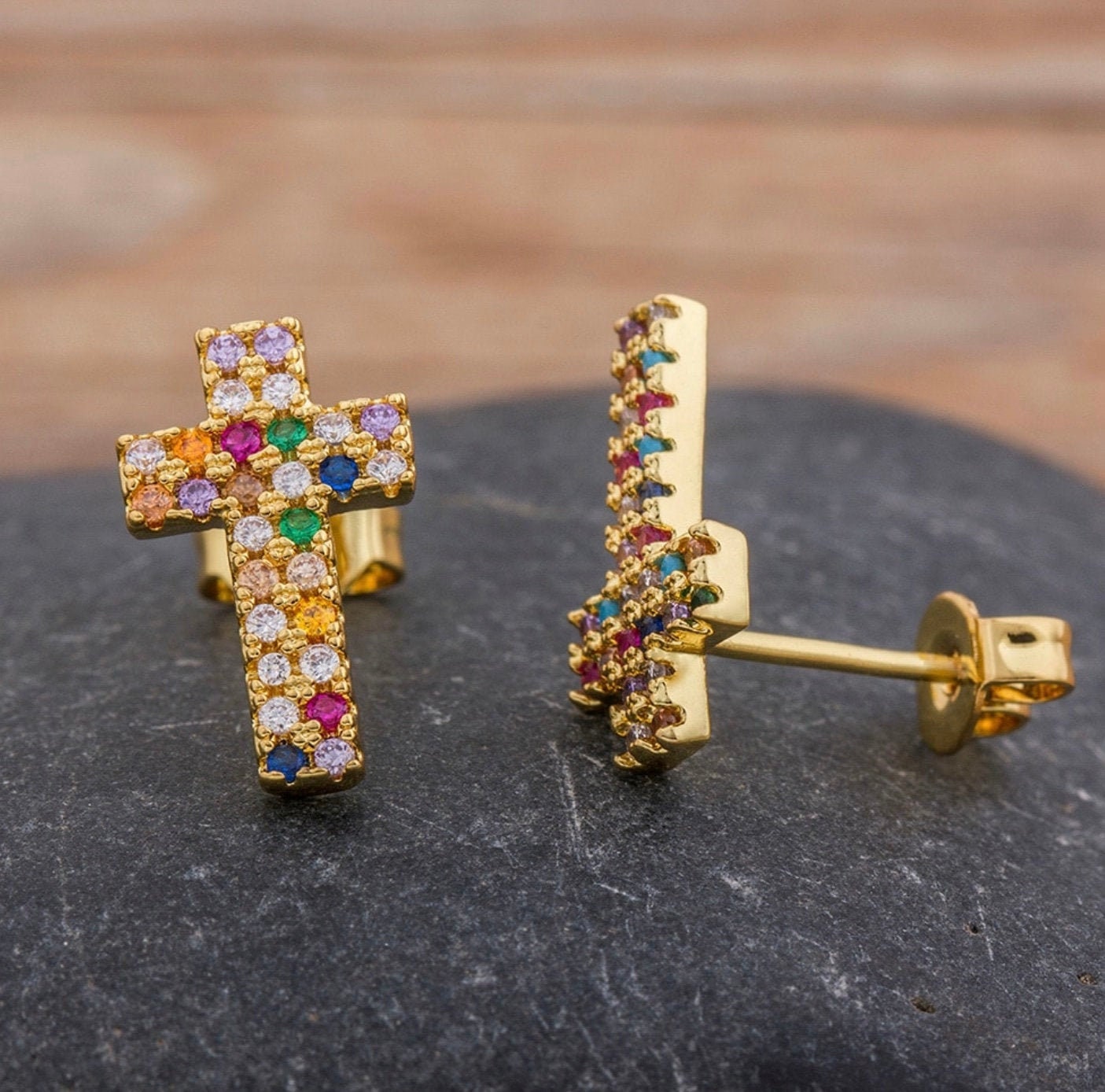 Gold-tone cross stud earrings with rainbow rhinestone inlay, close-up side view.
