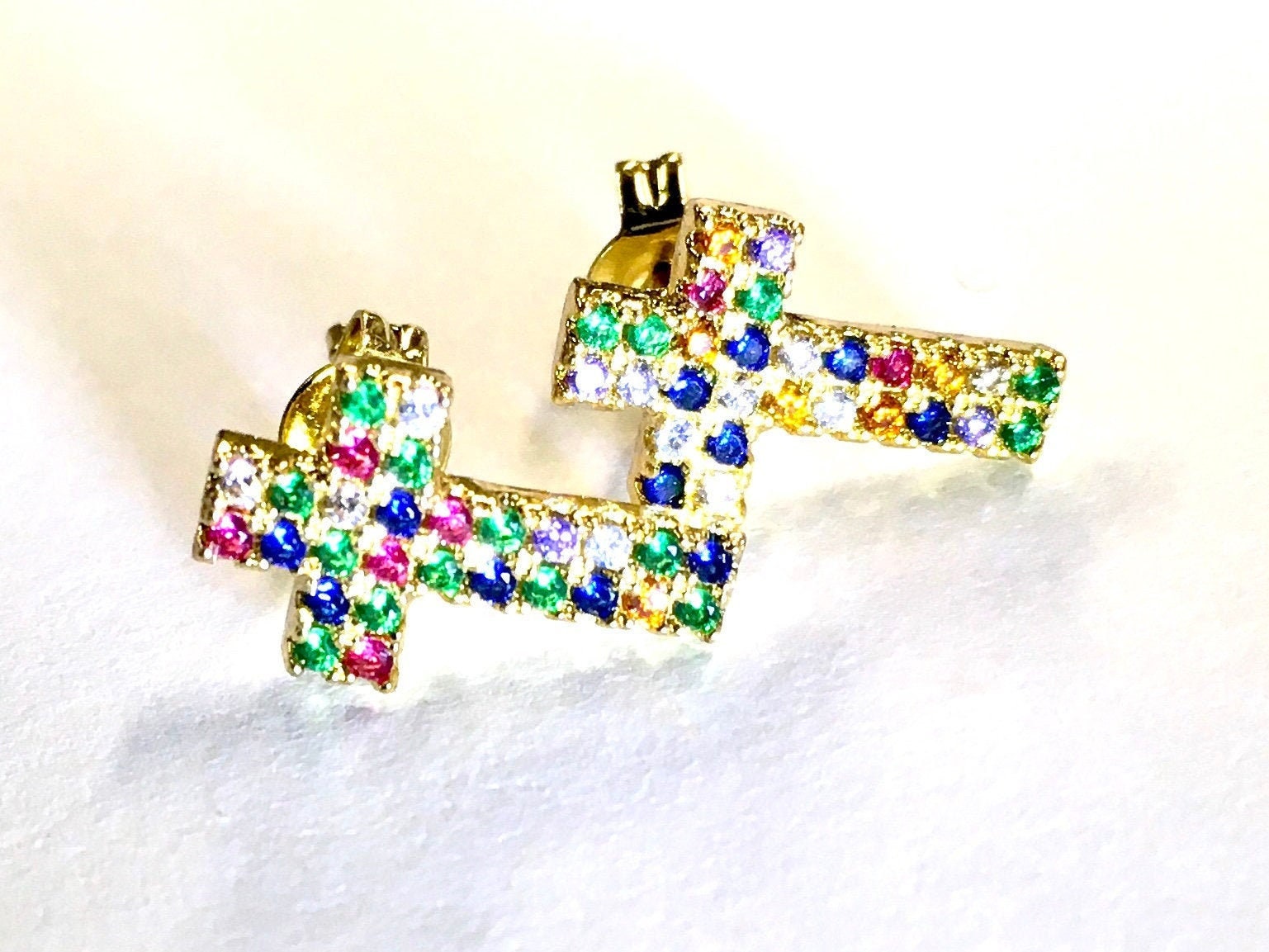 Gold-tone cross stud earrings with rainbow rhinestone rows, angled pair view.