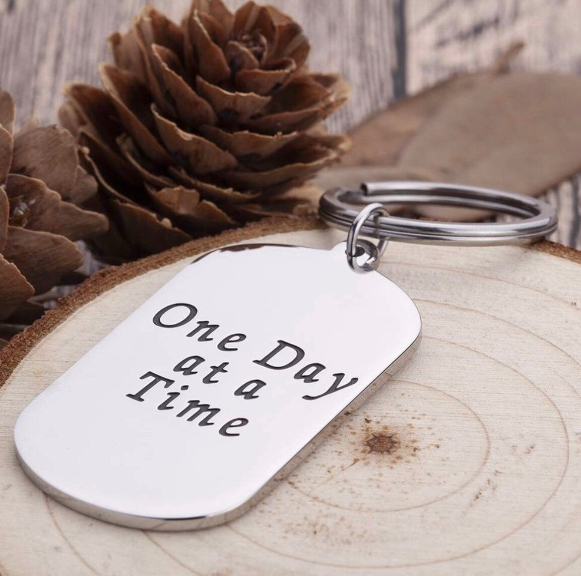 Silver dog tag keychain with 'One Day at a Time' prayer text and metal loop