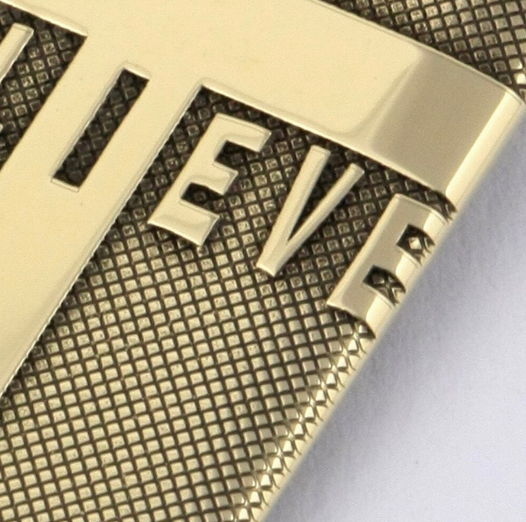 Close-up of gold-tone pendant showing engraved 'BELIEVE' text and cross detail