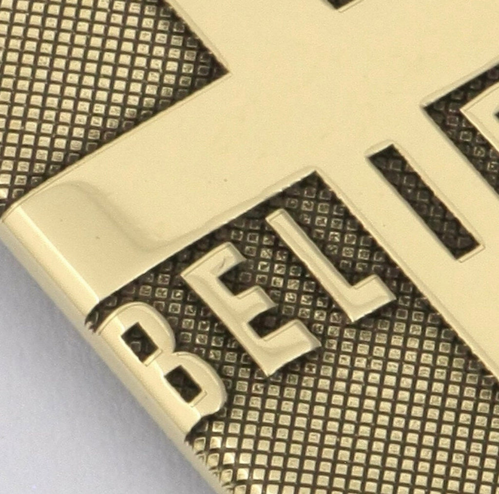 Gold-tone pendant close-up with 'BELIEVE' engraved letters over cross-hatch texture