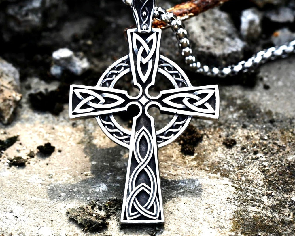 Silver Celtic knot cross pendant necklace on a chain, hanging over a rough stone surface