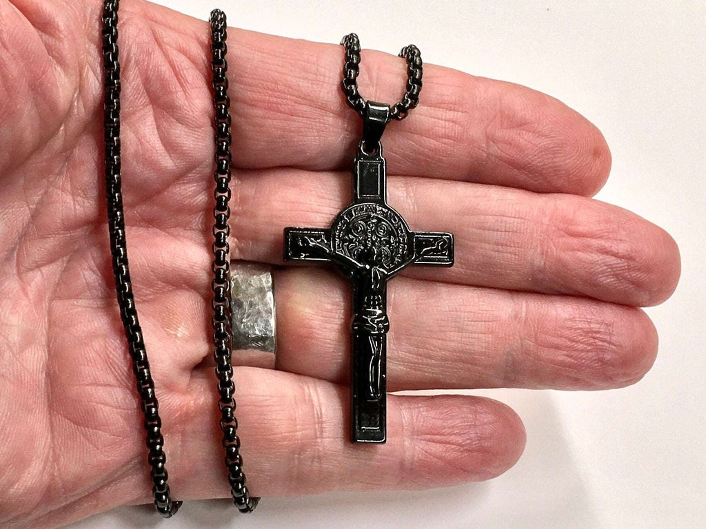 Black crucifix pendant necklace with bead chain, shown in hand