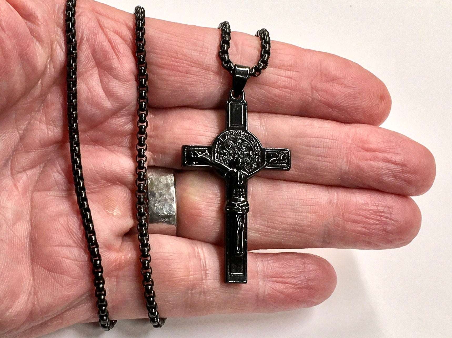 Black crucifix pendant necklace with bead chain, shown in hand