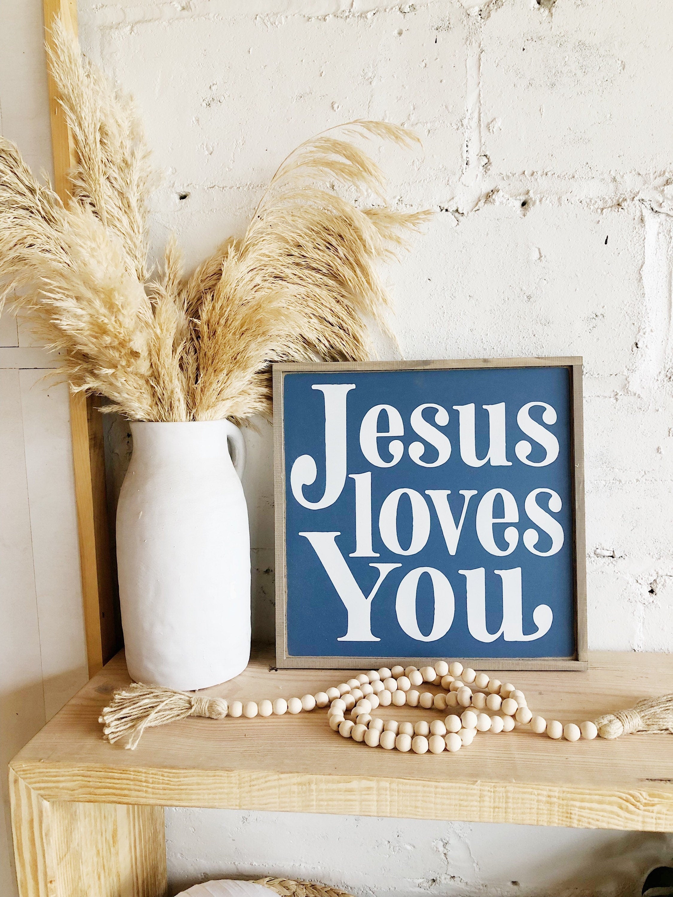 Wood framed wall sign reading “Jesus loves you” with blue lettering