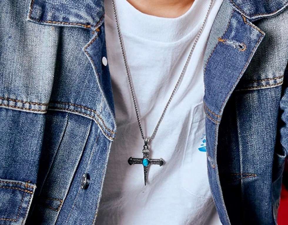 Cross pendant necklace worn under denim jacket; turquoise oval stone on hammered cross
