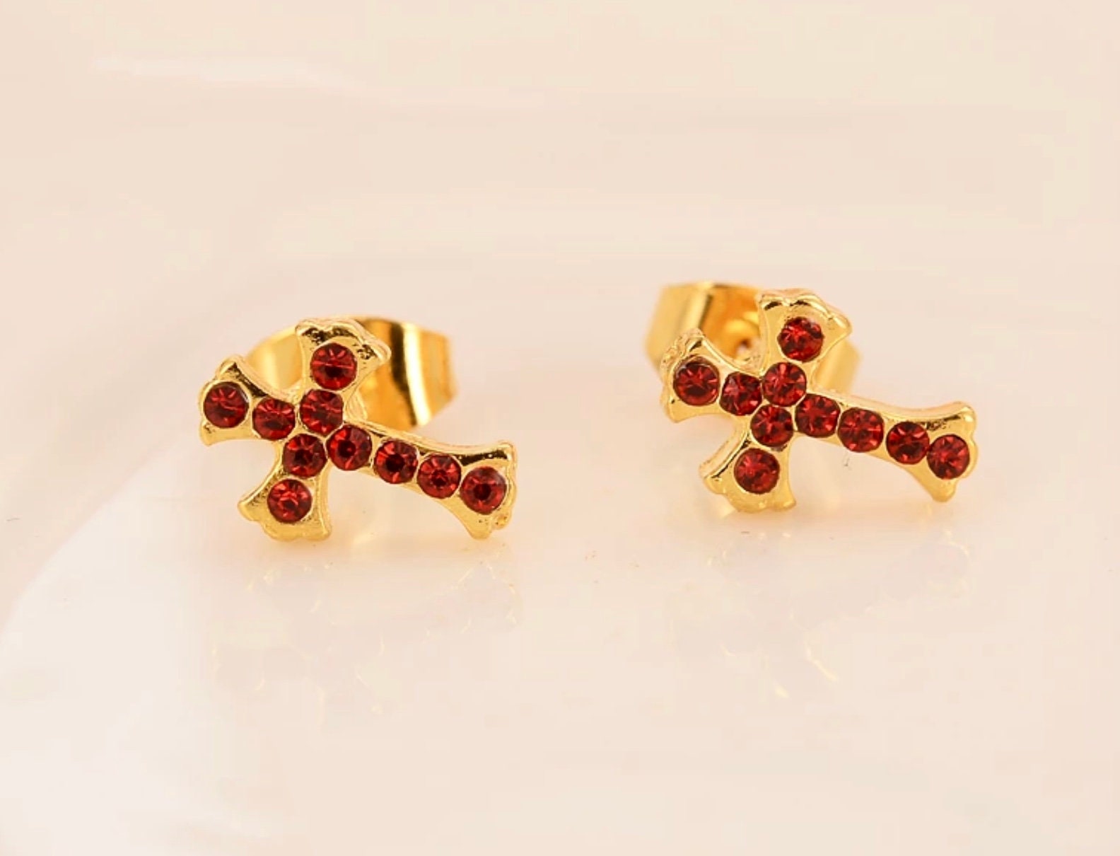 Gold cross stud earrings with red CZ stones, shown from the front on a light background