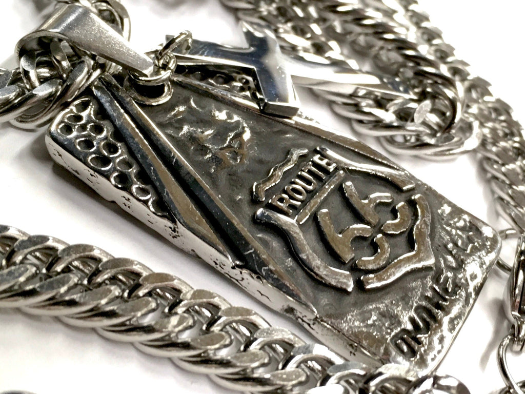 Close-up dog tag pendant with raised cross, Route 66 logo, and curb chain links
