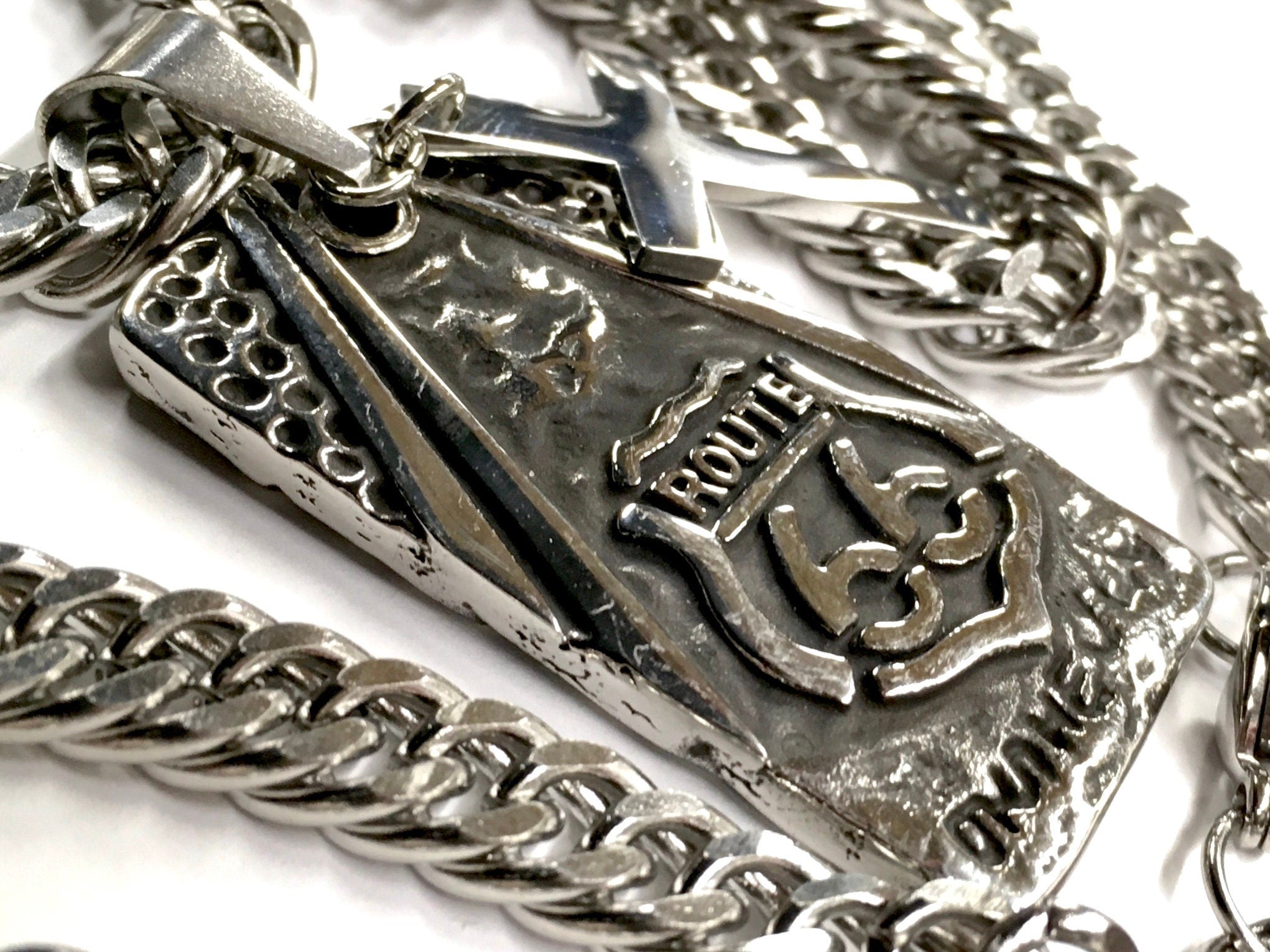 Close-up dog tag pendant with raised cross, Route 66 logo, and curb chain links
