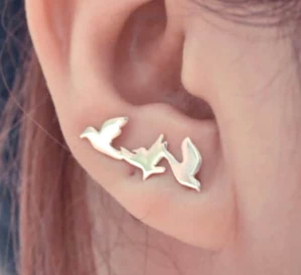 Gold dove and peace branch ear climber stud earrings on an ear, close-up