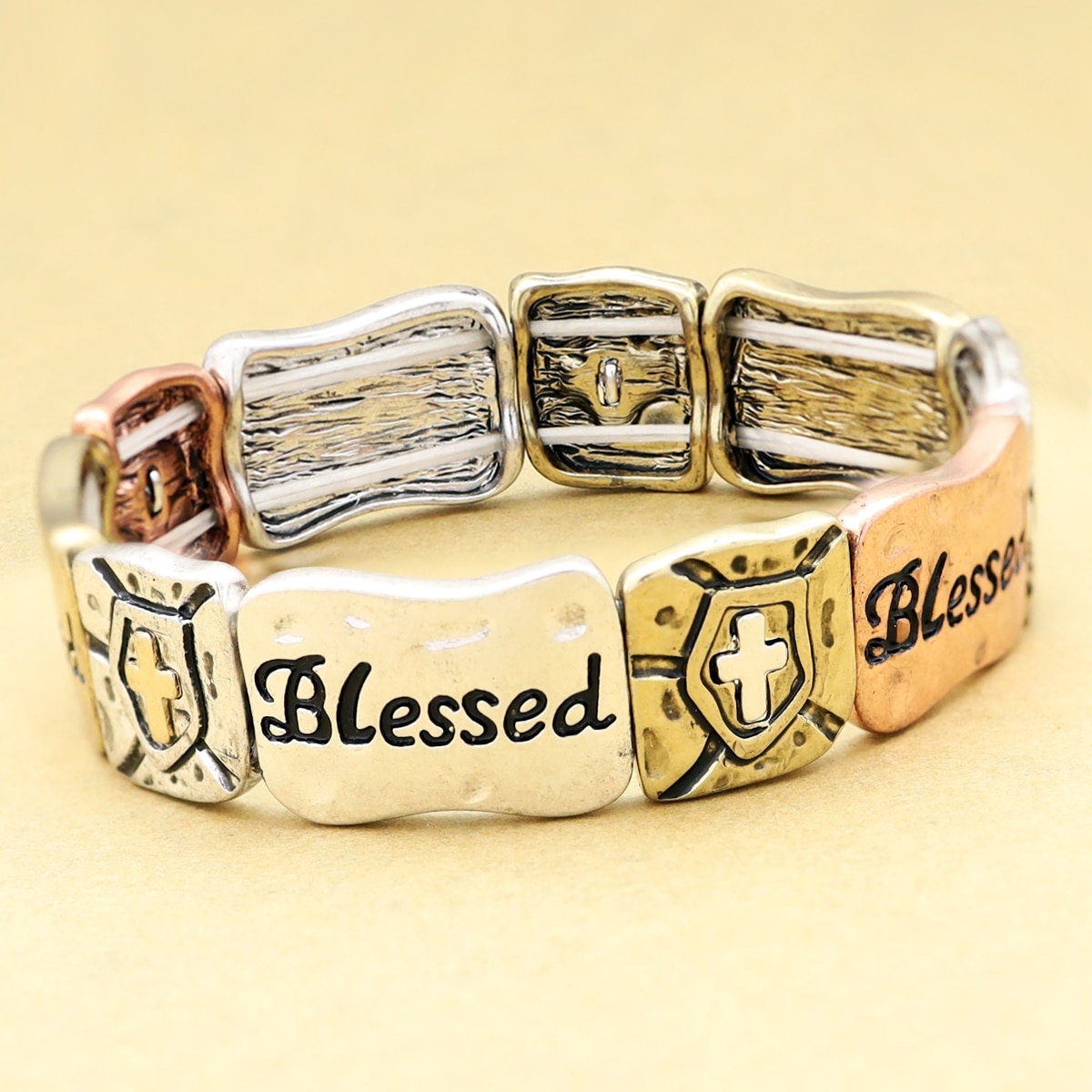 Gold-tone stretch bracelet cuff with three linked panels, cross emblem, and “Blessed”