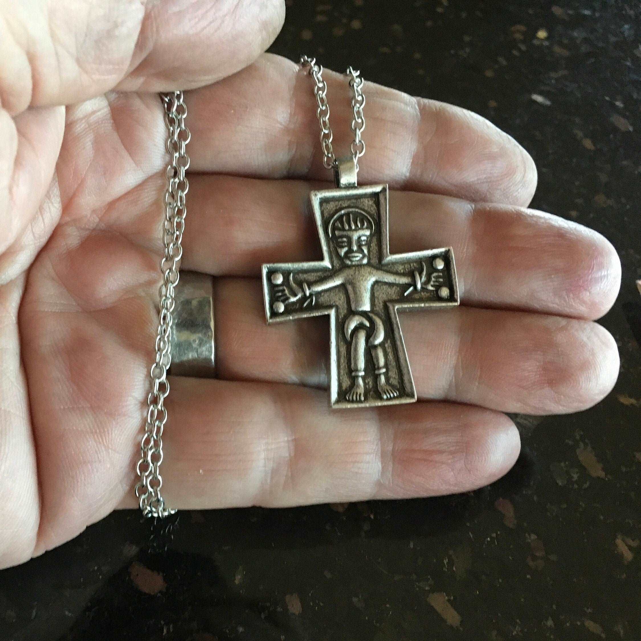Silver cross pendant on chain, Jesus figure centered, held in hand