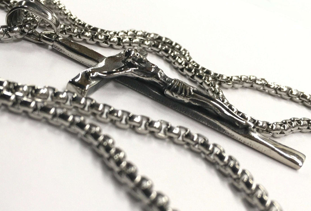 Stainless steel crucifix pendant on link chain, close-up of Jesus relief and cross.