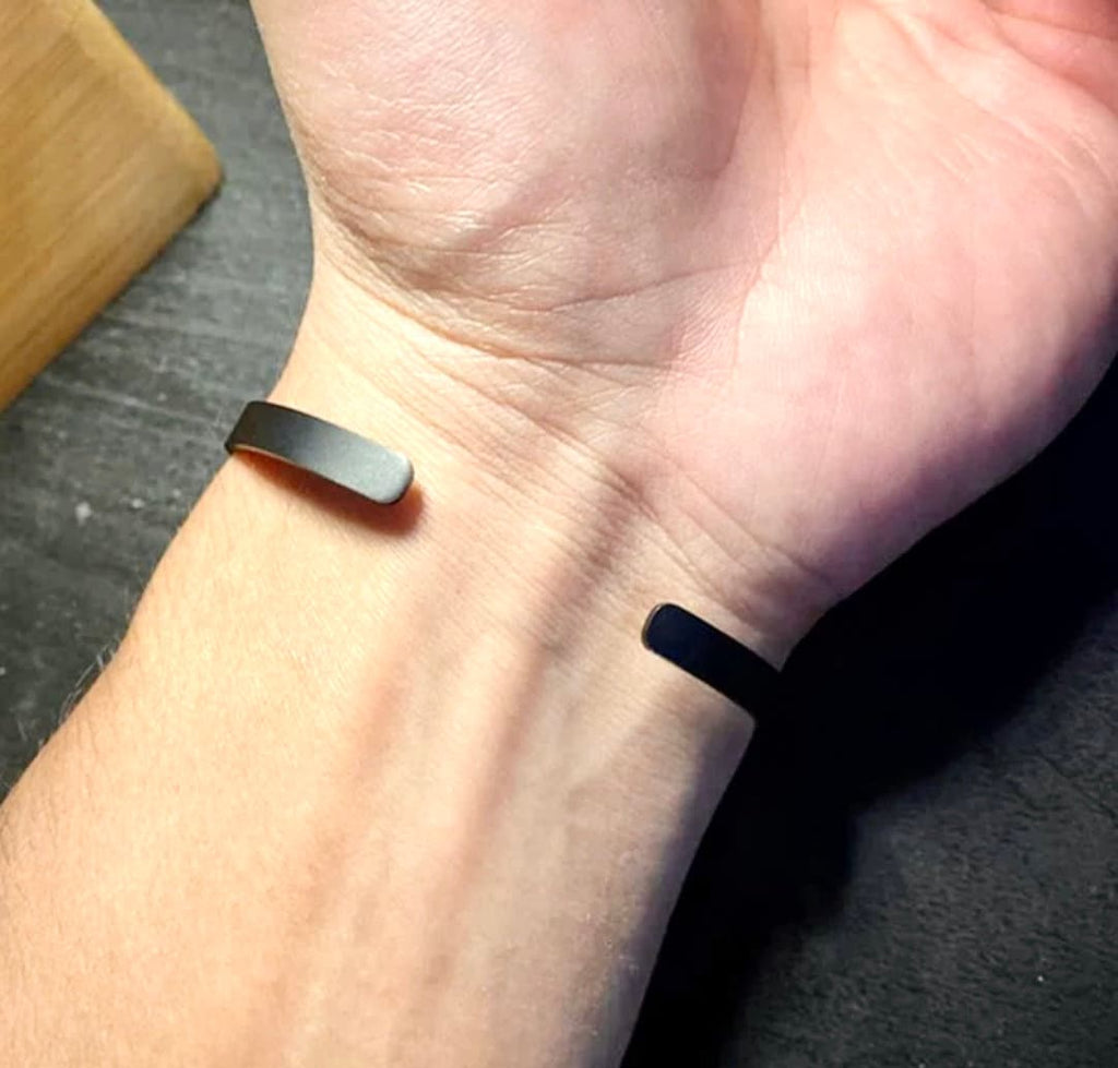 Pair of slim stainless steel cuff bracelets on wrist, one dark, one silver