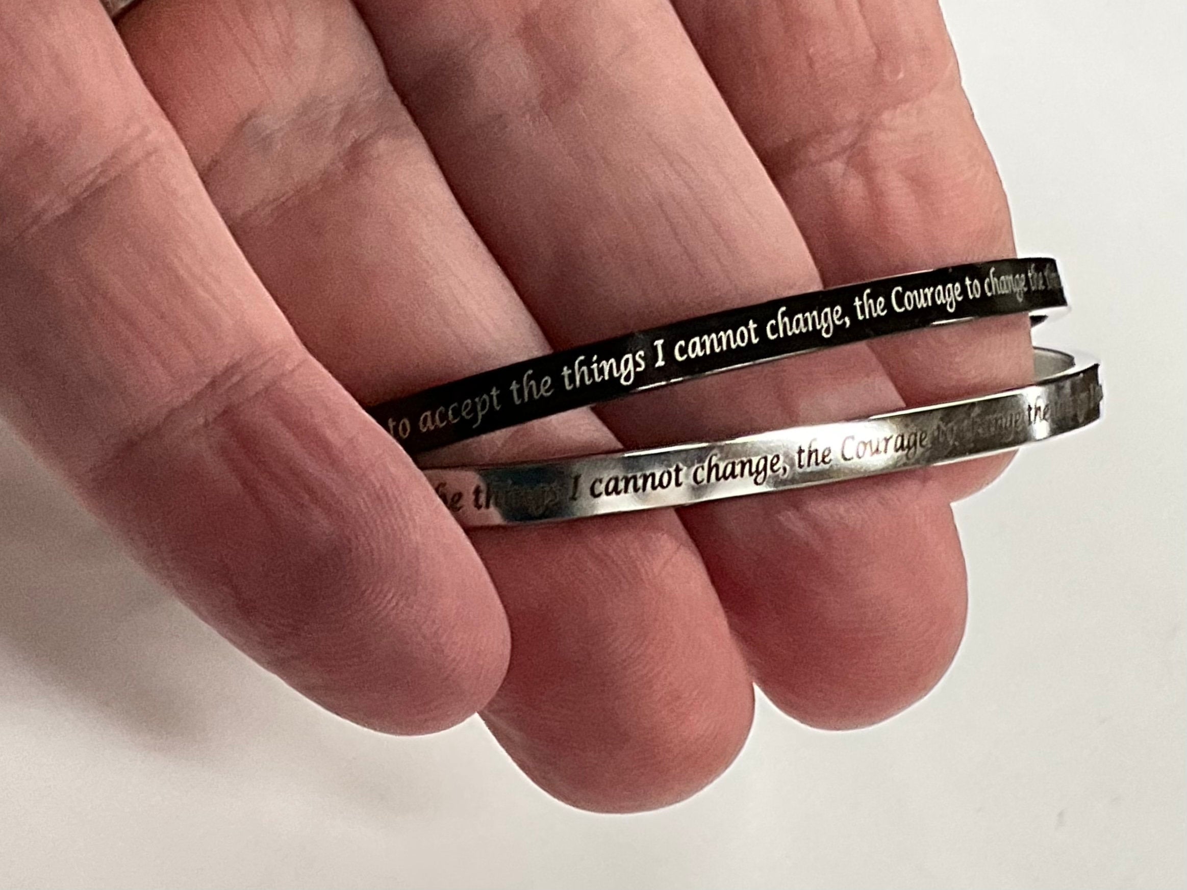Thin stainless steel cuff bracelets on hand, engraved serenity prayer text, cross motifs