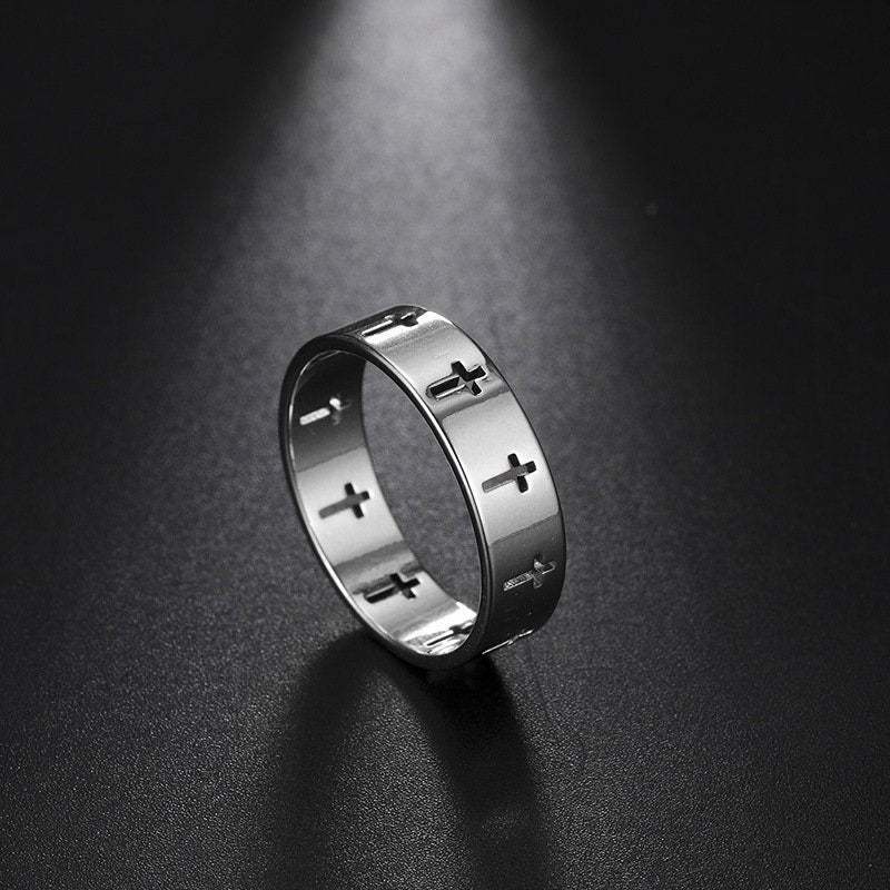 Stainless steel cross band ring, front view with raised cross details on a dark surface