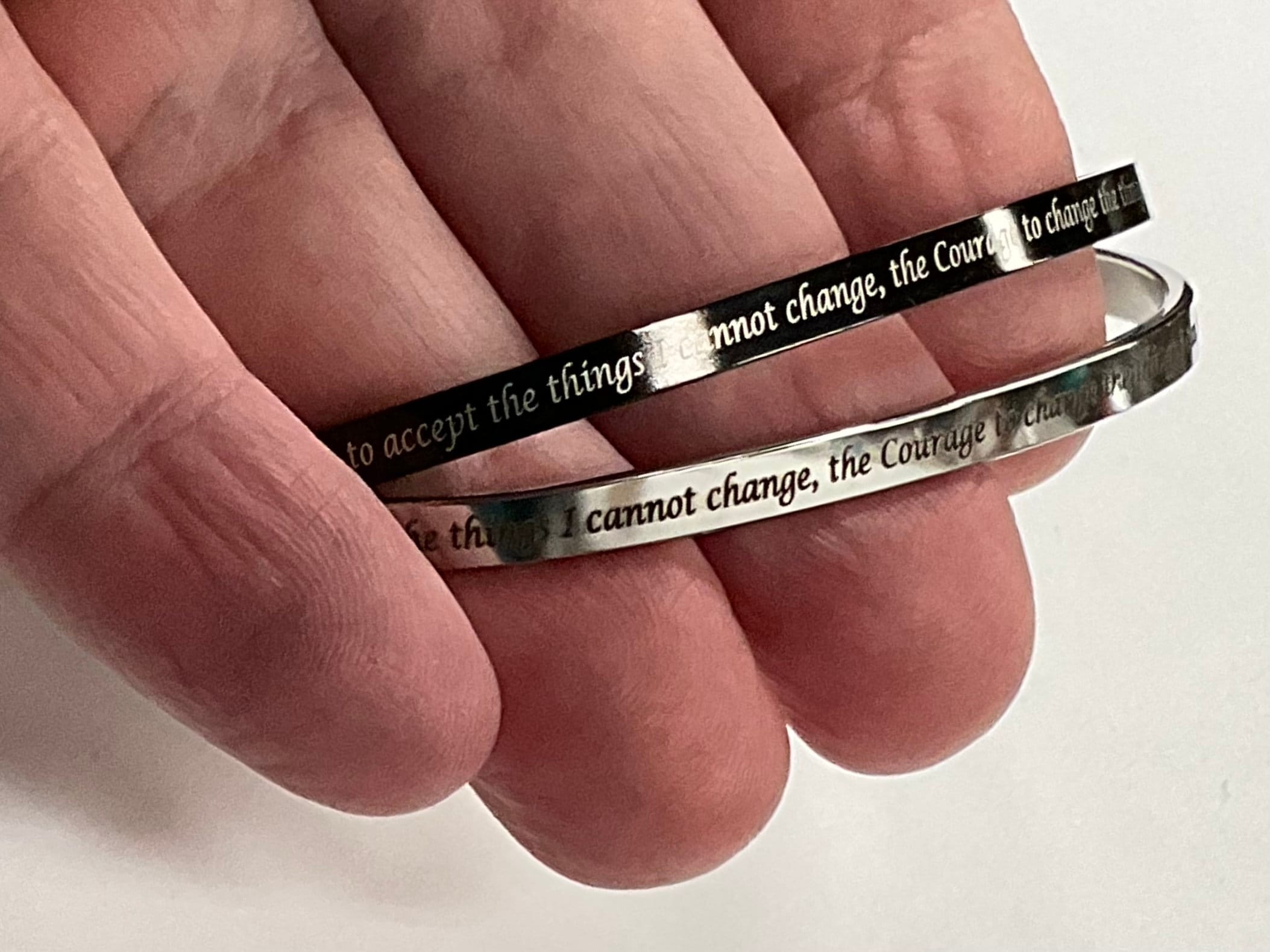 Thin stainless steel cuff bracelets on hand with engraved prayer line and cross motifs