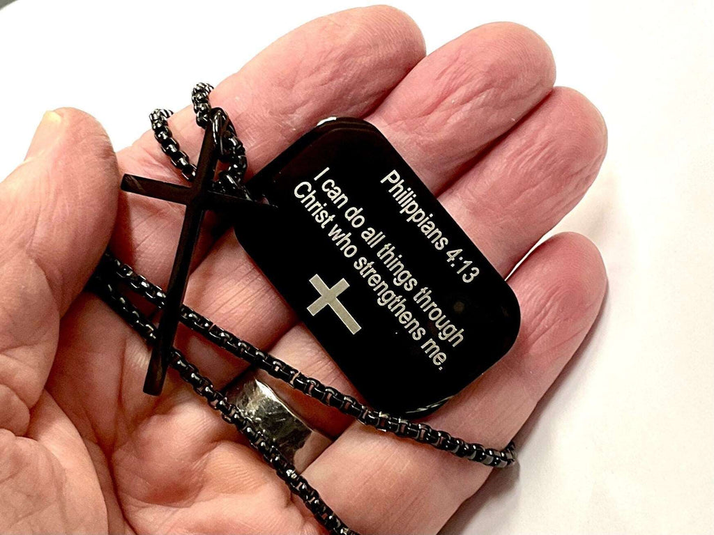 Black dog tag cross necklace held in hand; Philippians 4:13 quote on pendant