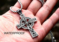 Silver Celtic knot cross necklace pendant on a box chain, held in an open hand