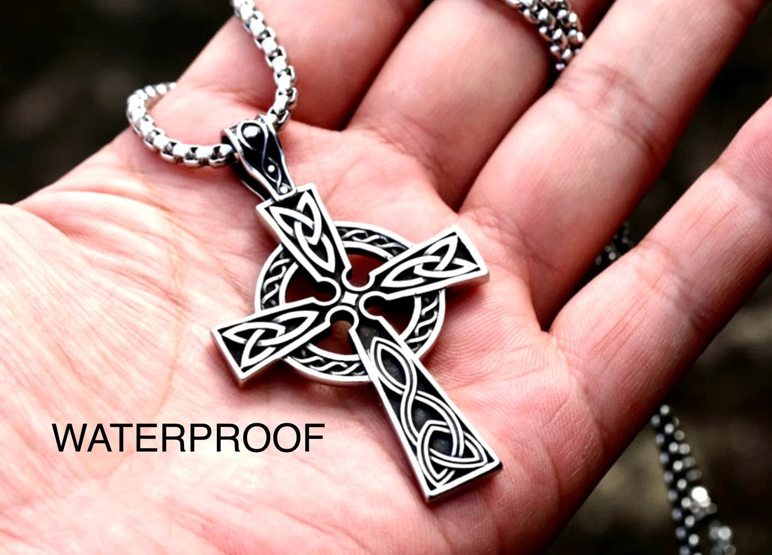 Silver Celtic knot cross necklace pendant on a box chain, held in an open hand
