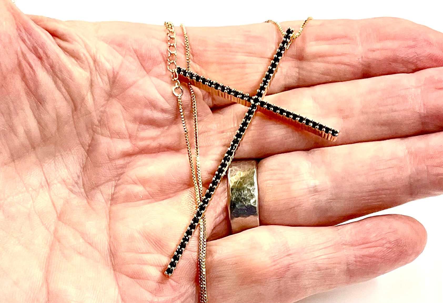 Cross necklace with black rhinestone crucifix and gold chain, close view on palm