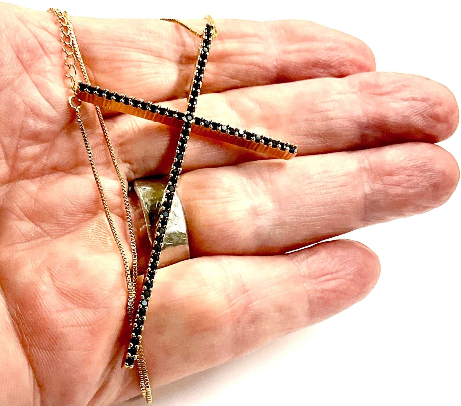 Crucifix cross necklace shown on hand, black rhinestone bar with gold chain links