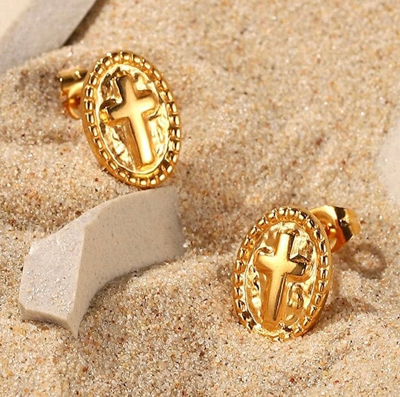 Gold oval cross stud earrings on sand with stones