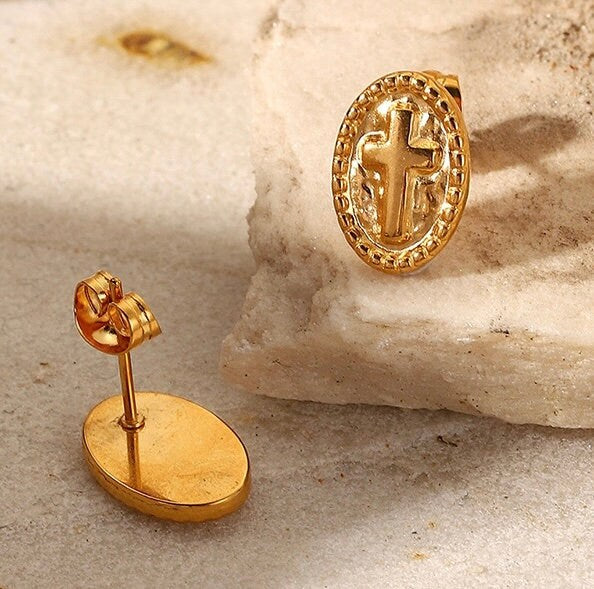 Gold oval cross stud earrings lying on light stone surface