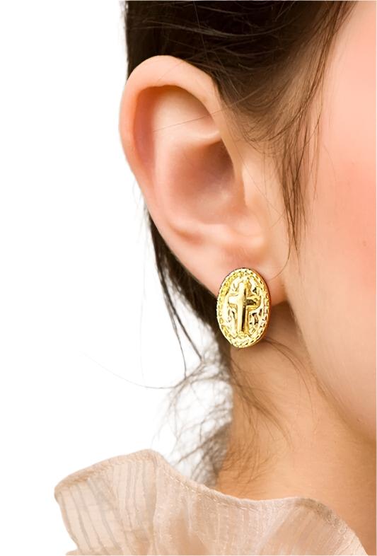 Gold oval cross stud earrings on an ear with visible post back