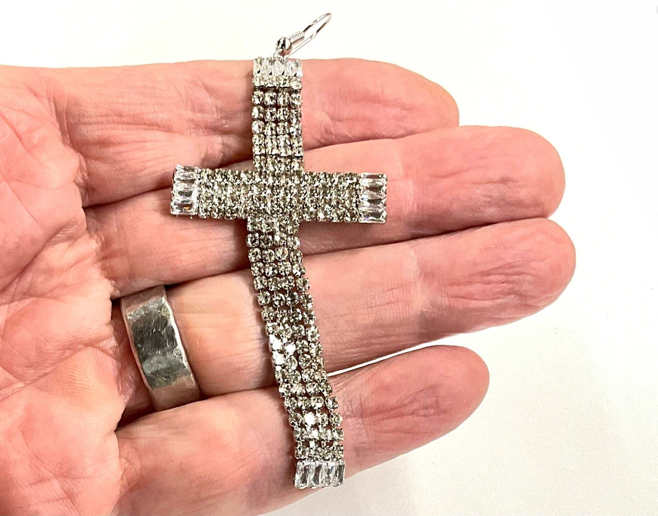 Rhinestone cross dangle earring held in hand, long cross with row stones and hook