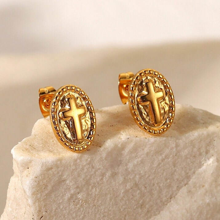 Gold oval cross stud earrings resting on white textured stone