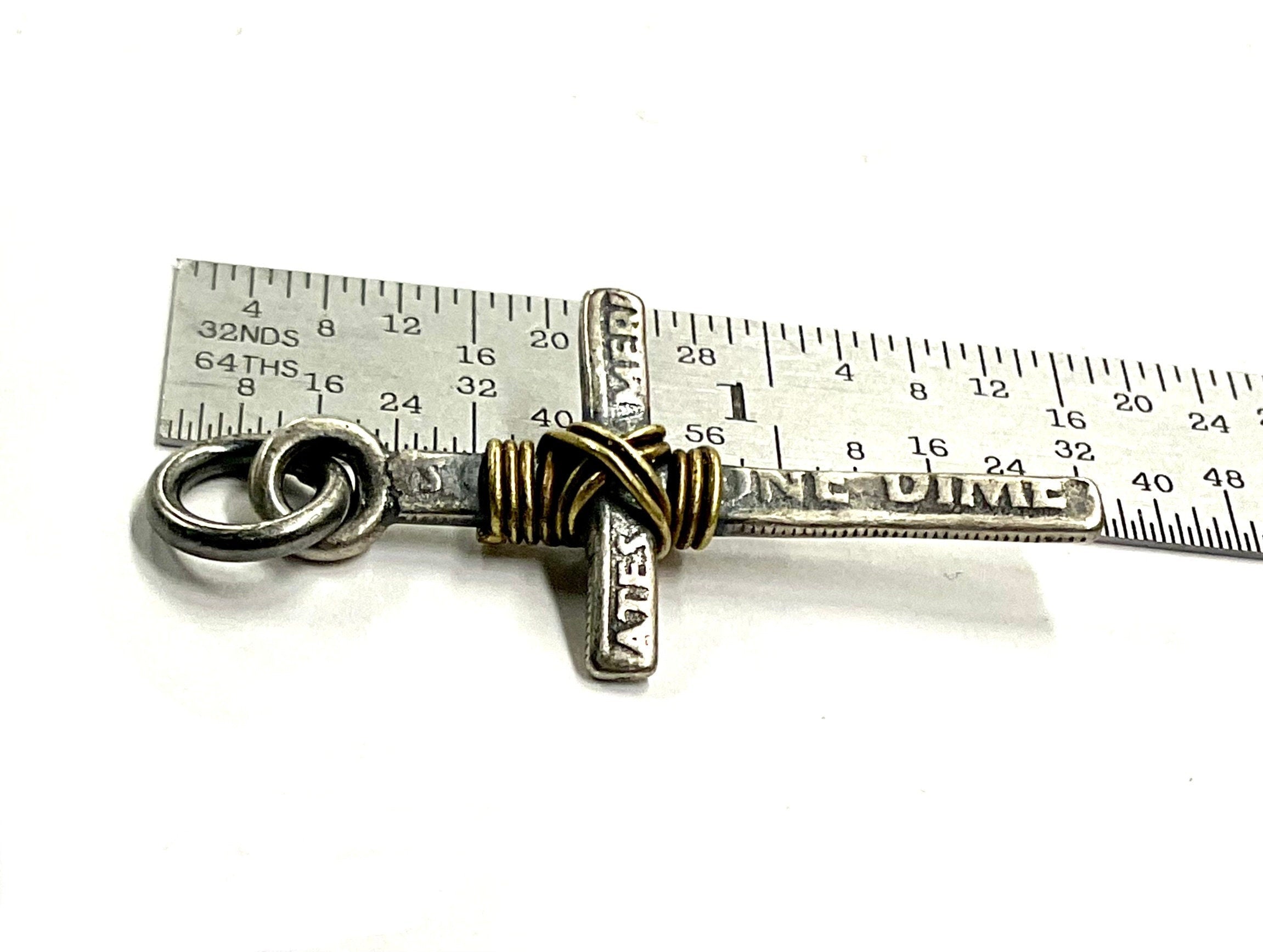 Silver-tone cross necklace pendant with gold wire wrap detail shown with a ruler scale