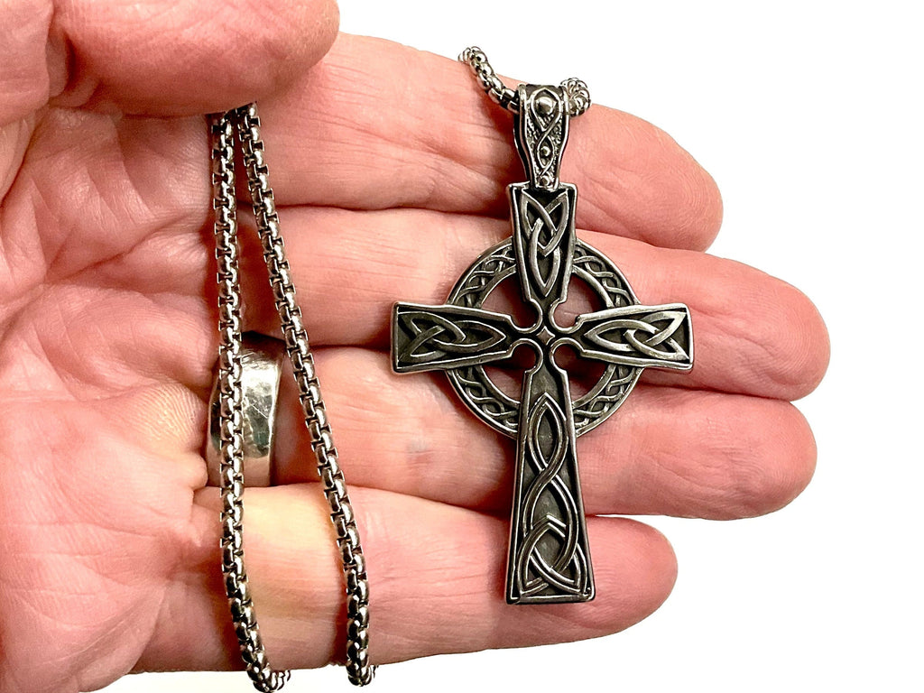 Silver Celtic knot cross necklace pendant with curb-style chain in a palm