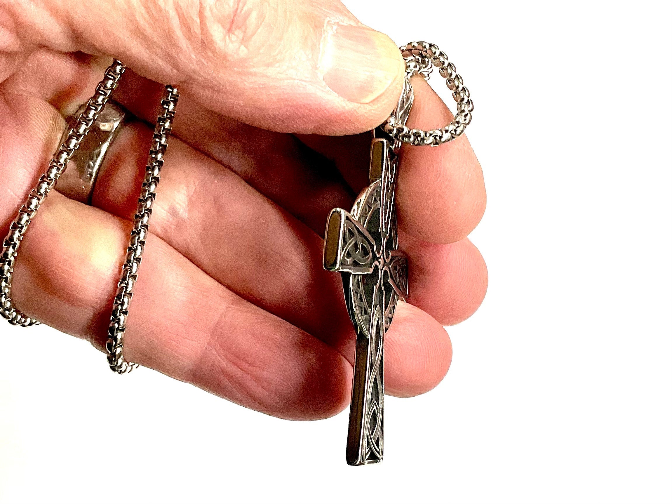 Silver Celtic knot cross pendant on a chain, shown close in a hand