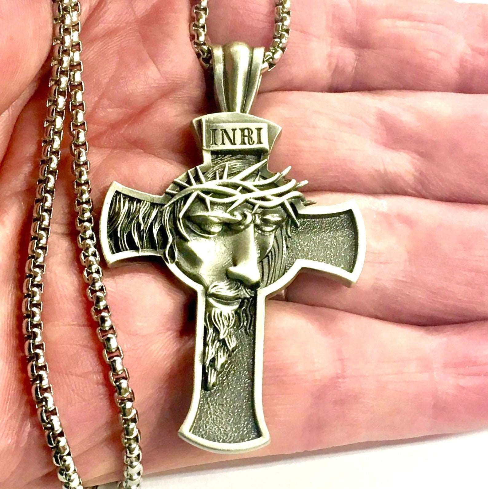 Close-up cross pendant necklace showing Jesus profile, INRI plate, and chain links