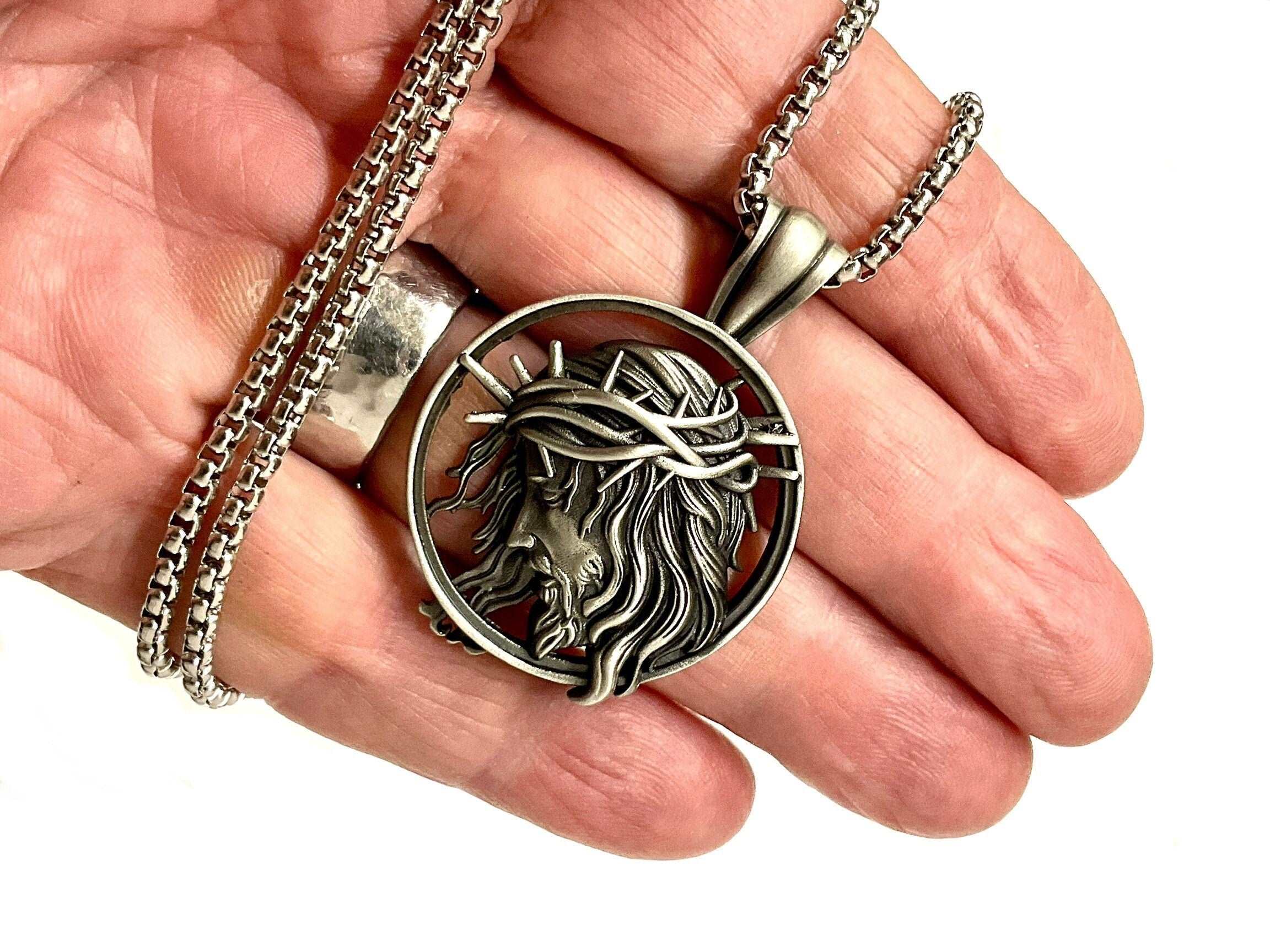 Religious pendant necklace, circular Jesus face medallion on chain, held in hand.