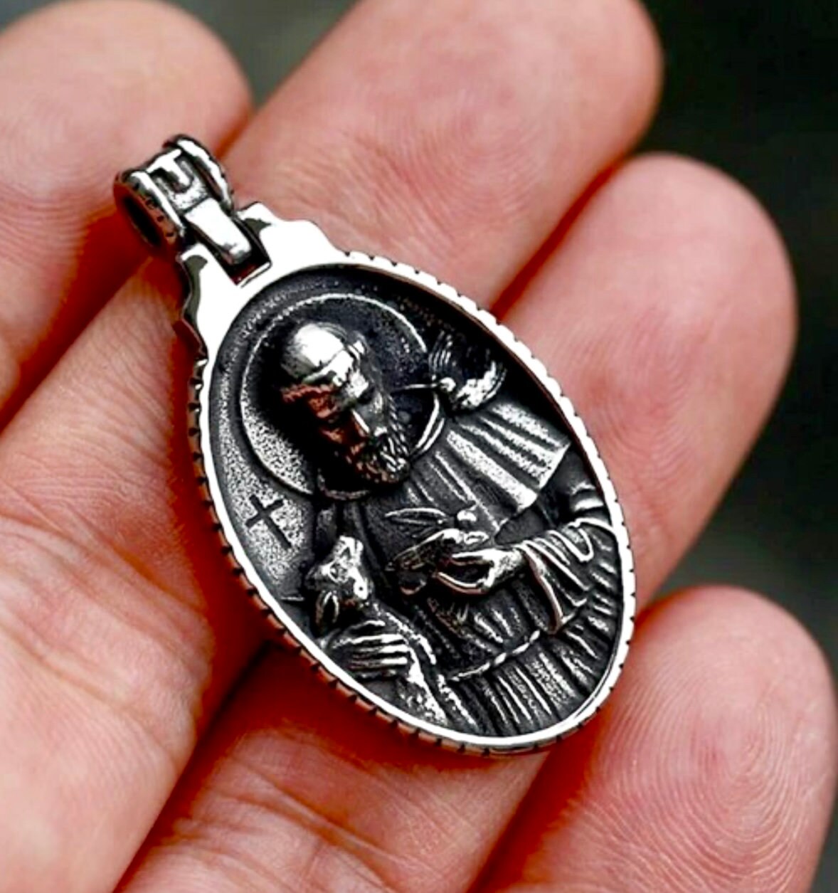 Oval metal religious medal pendant on silver chain, held in hand