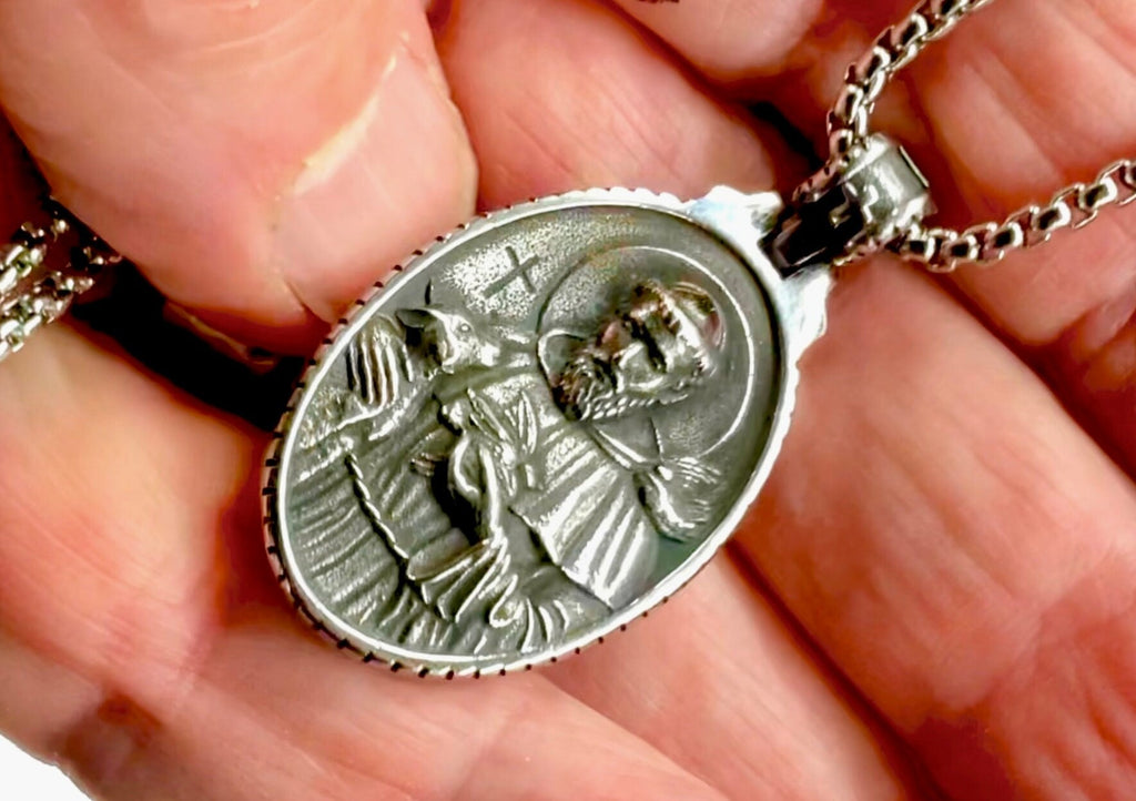 Oval metal religious medal pendant on chain, close-up in hand