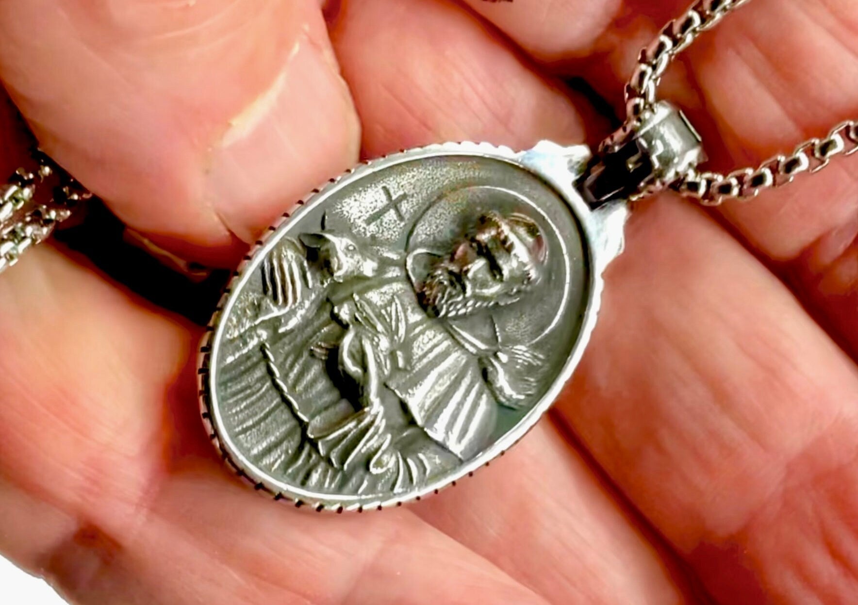 Oval metal religious medal pendant on chain, close-up in hand