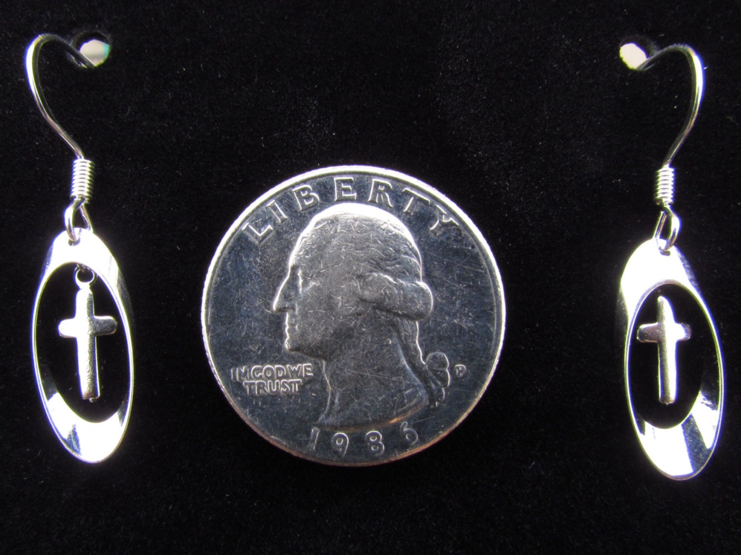 Silver cross earrings with oval drops, shown beside a coin for scale