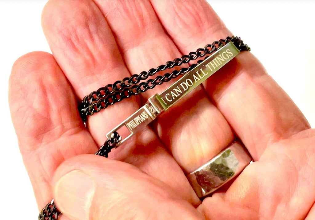 Black chain cross necklace on hand, silver pendant with “I CAN DO ALL THINGS” engraving
