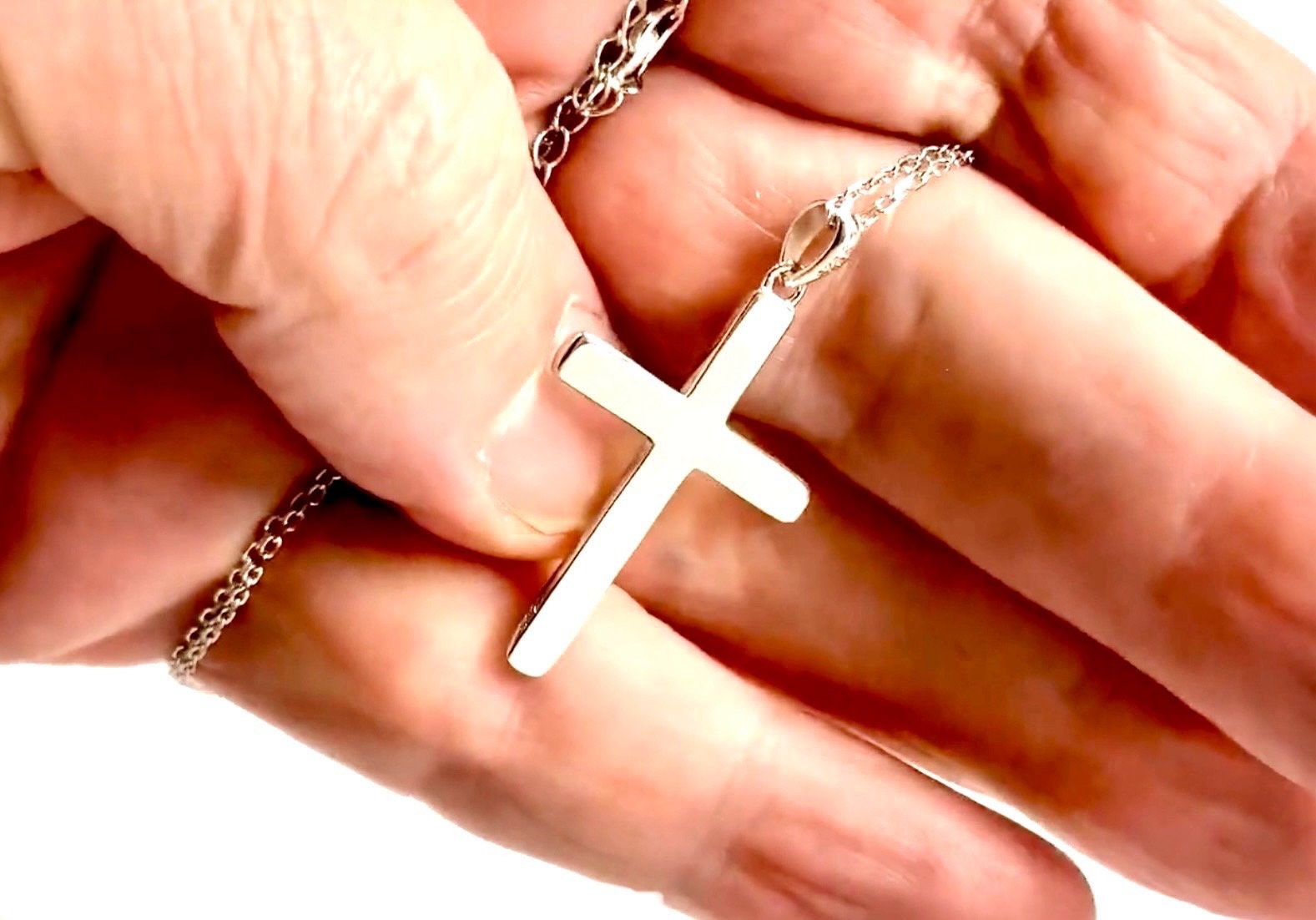 Sterling silver cross pendant necklace held in palm with chain visible