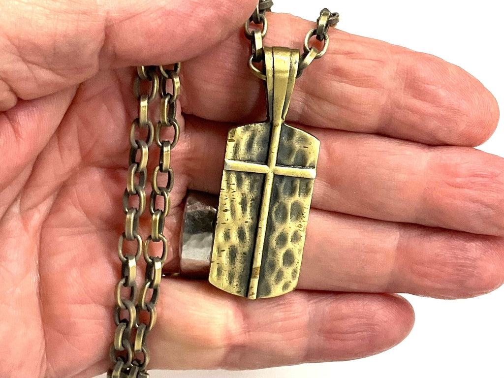 Gold-toned cross dog tag pendant necklace on chain, shown in open palm