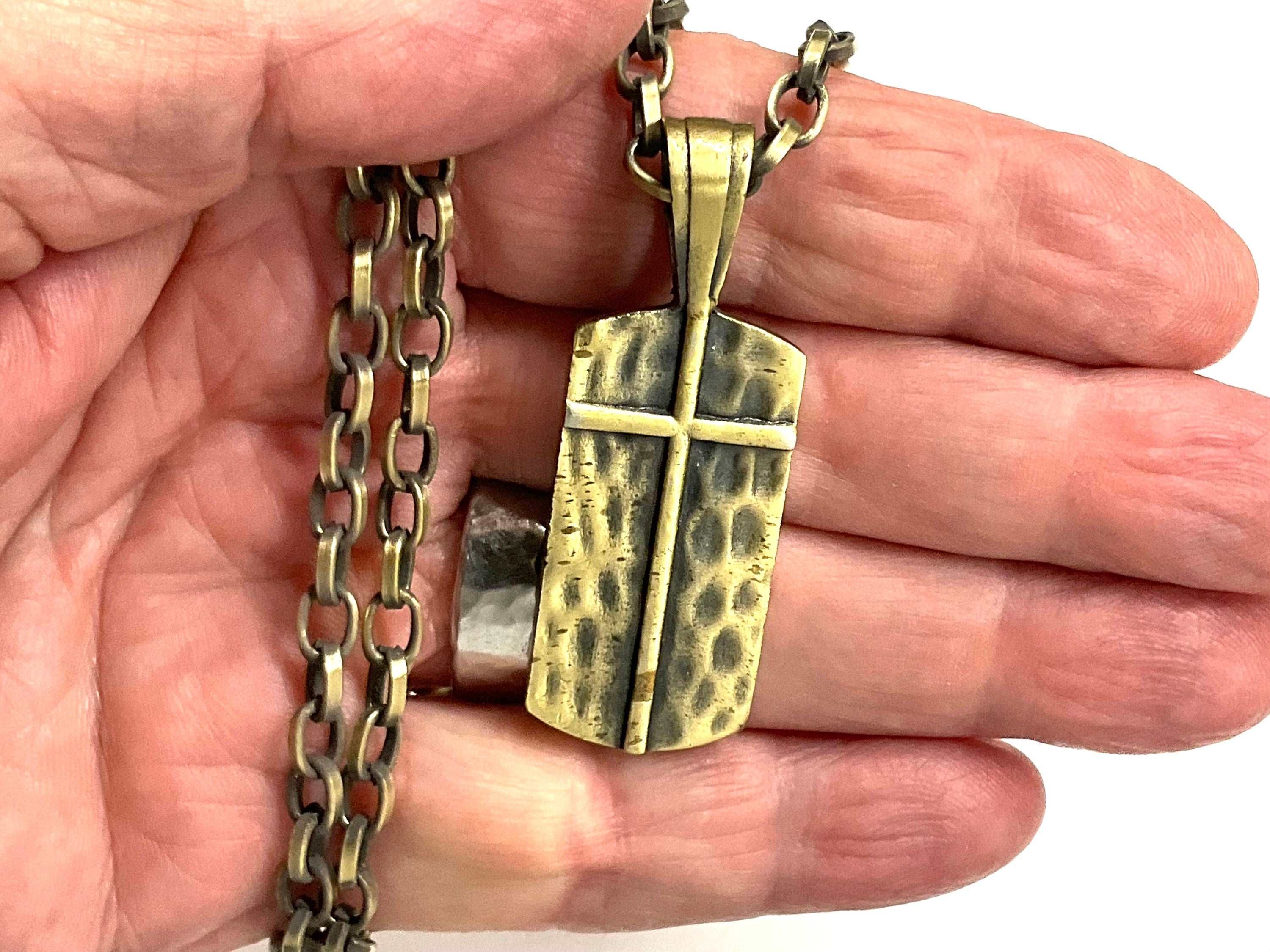 Gold-toned cross dog tag pendant necklace on chain, shown in open palm