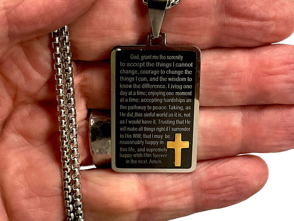 Black serenity prayer pendant with gold cross inset and silver chain, held in hand