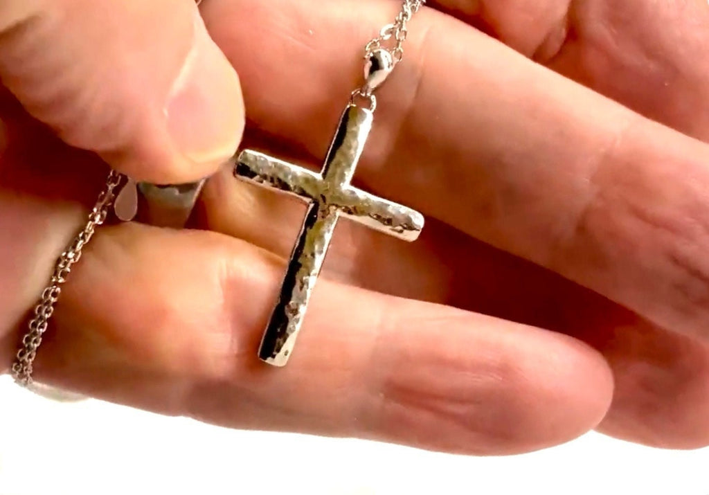 Sterling silver cross pendant necklace held in fingers on a chain