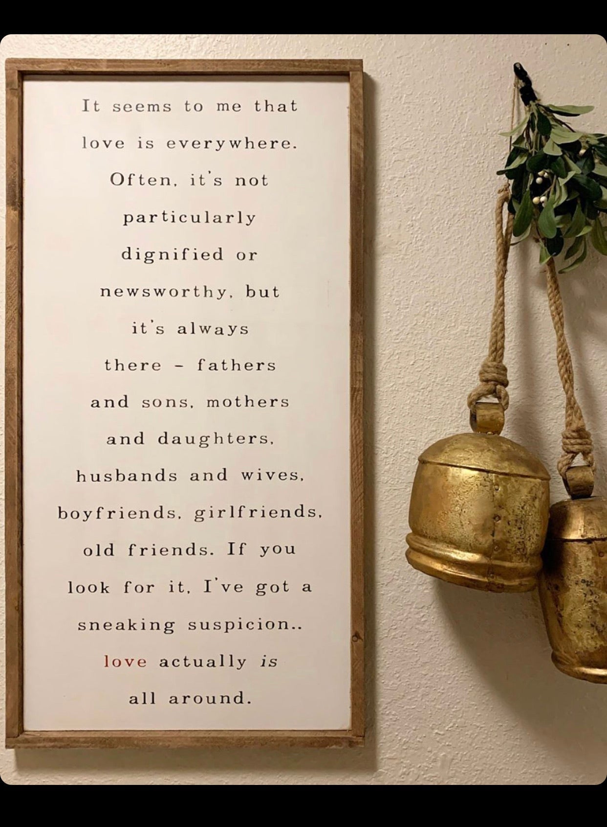 Framed wall hanging with wooden frame, vertical quote text, and brass bell ornament