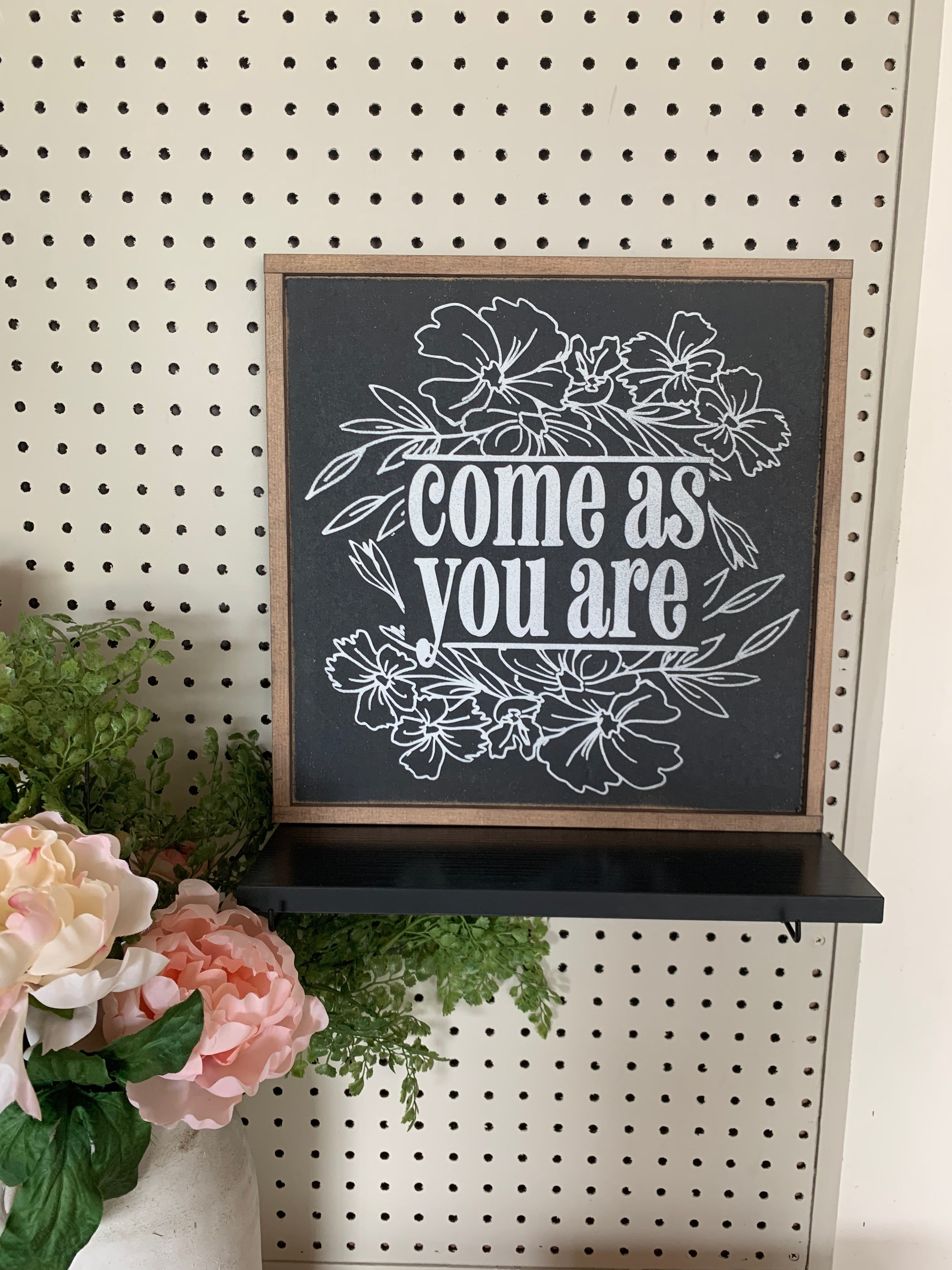 Framed floral wall sign with white script text reading “Come as you are”